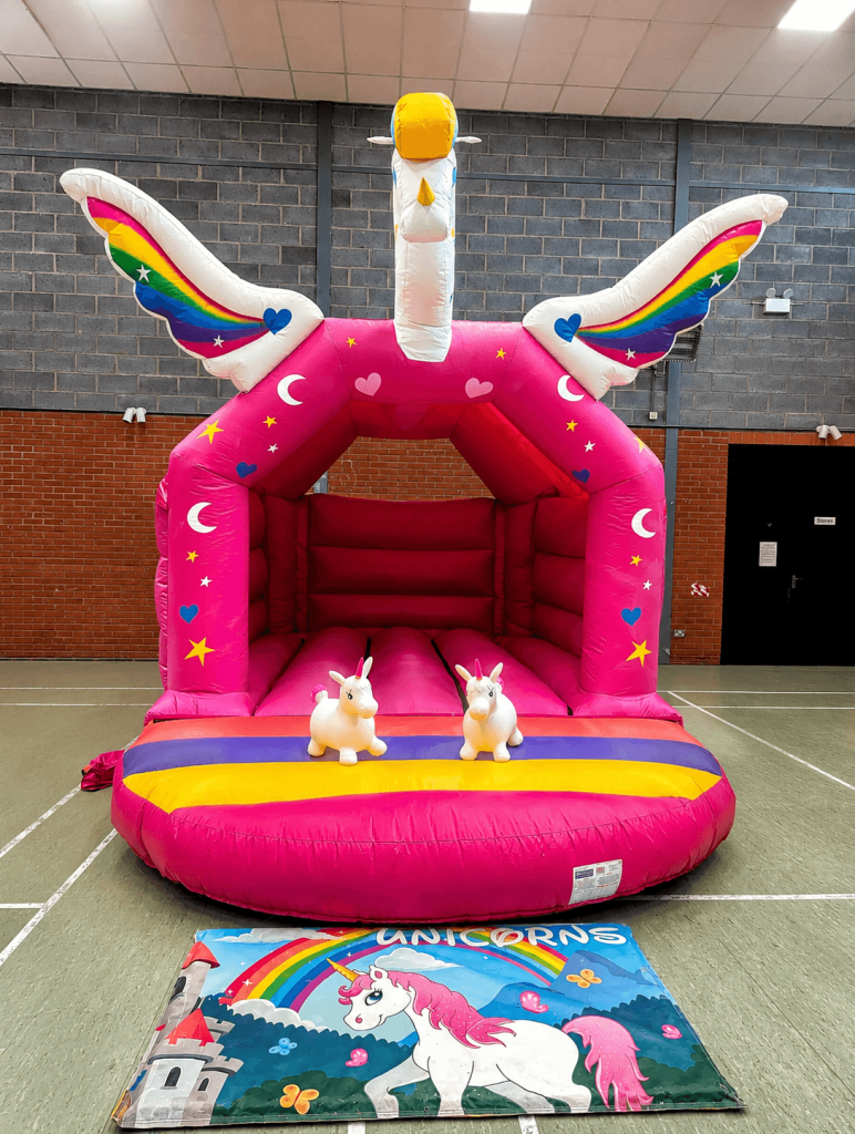 Pink unicorn bouncy castle with rainbow wings in a hall