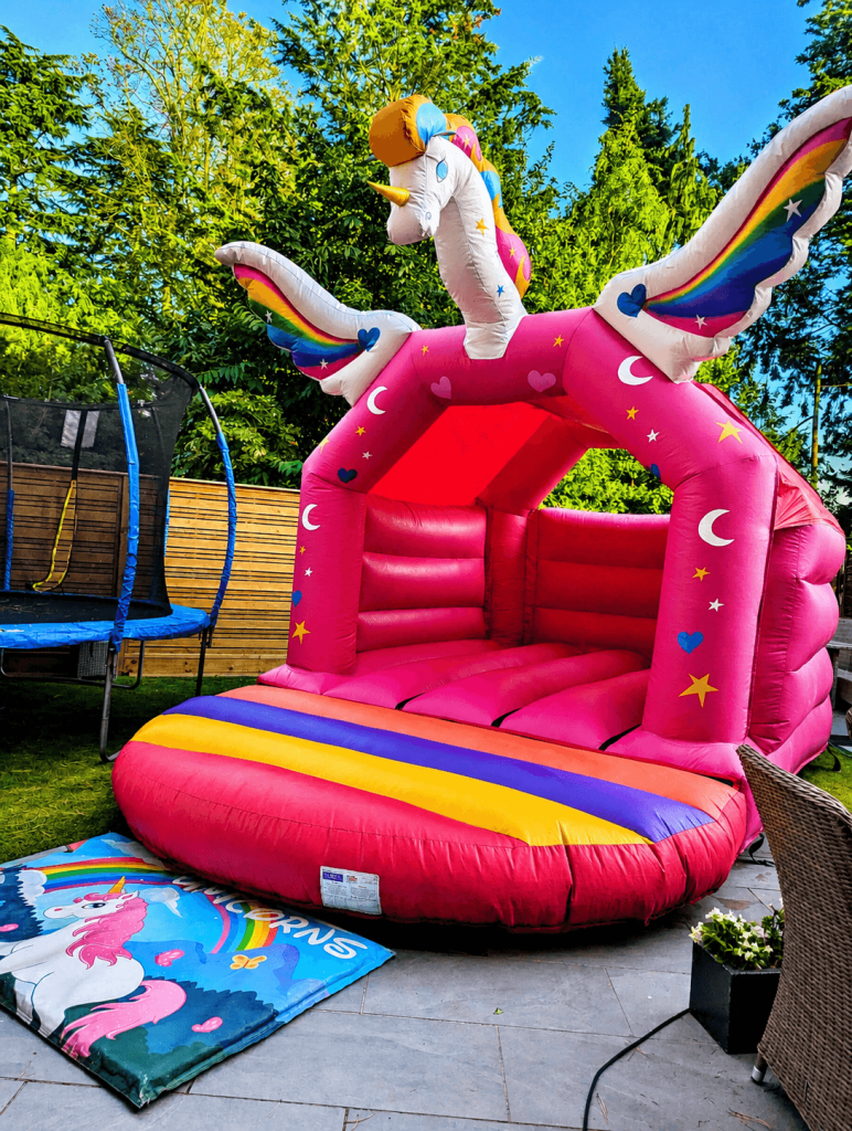 Pink unicorn bouncy castle with rainbow wings in a back garden
