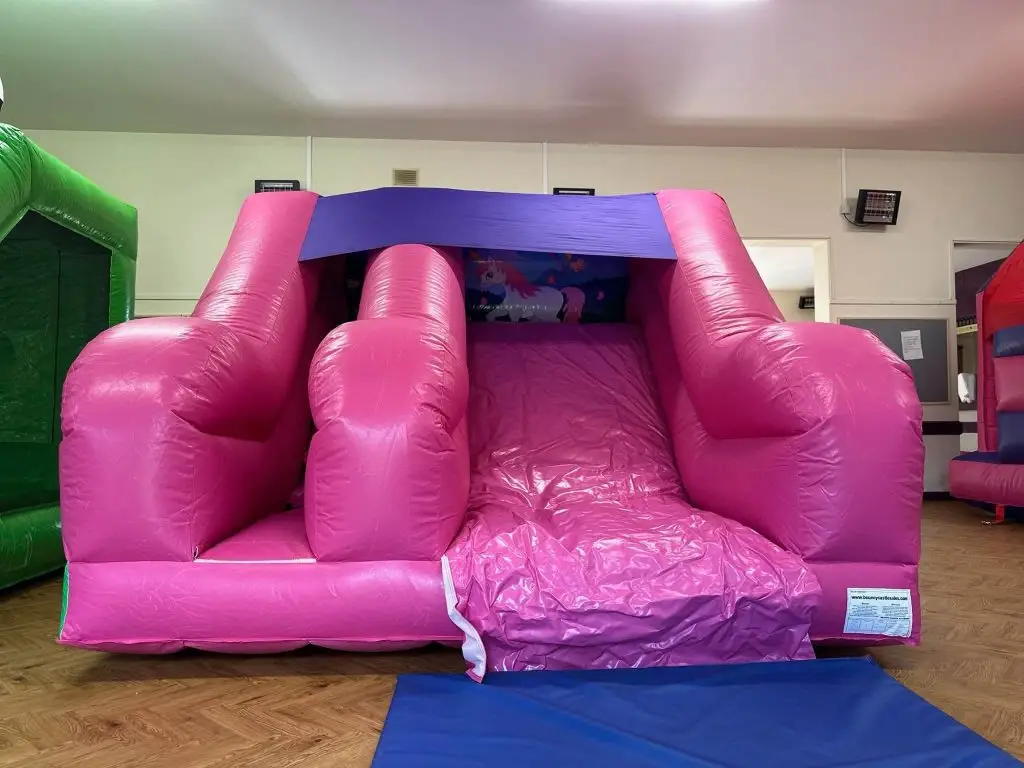 Pink bouncy castle with slide set up in a hall
