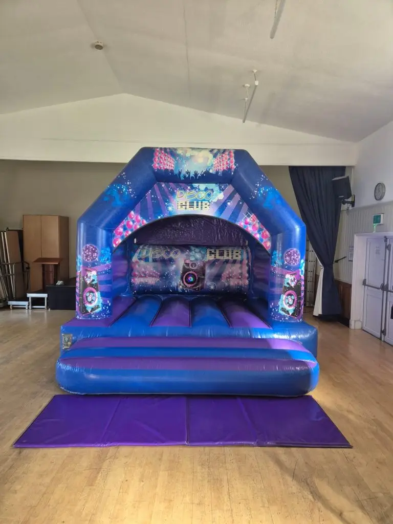 Disco Club bouncy castle in blue and purple with disco ball and speaker artwork, set up in a Colchester hall